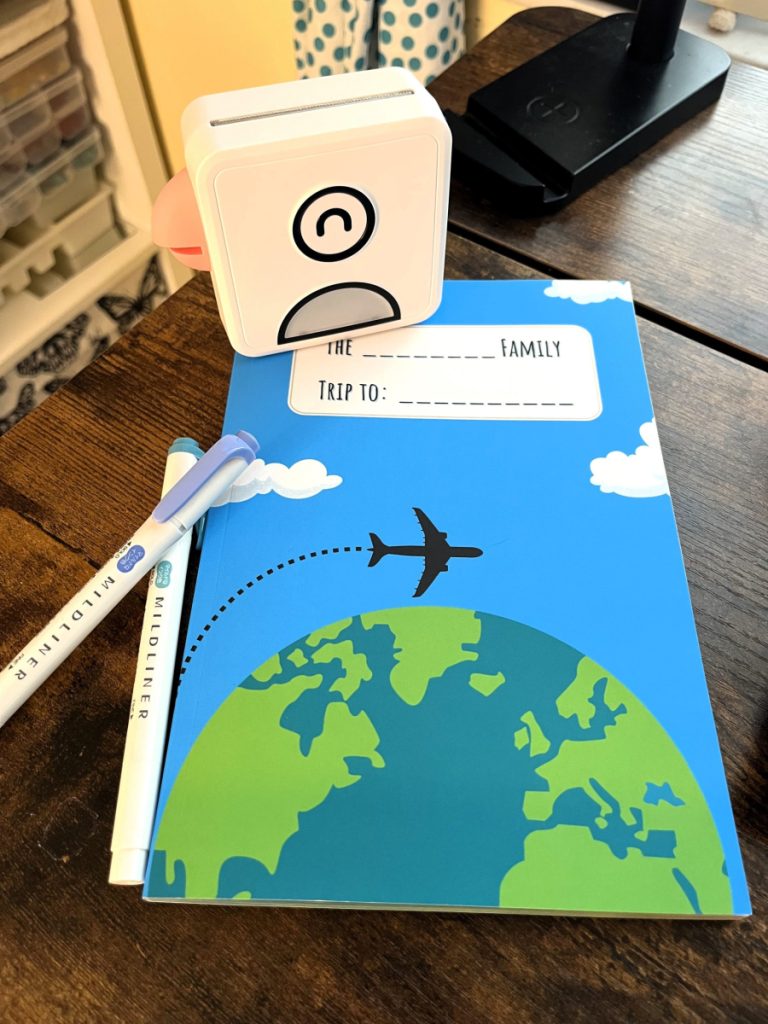 Photograph of 2 pens, the family travel journal and a PooliPrint portable printer.